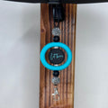 A car ornament with a bright turquoise ring, a black and turquoise  printed with 'Let them', black beads, rhinestone-embellished beads, and a silver lobster clasp, hanging on a dark wooden stand.