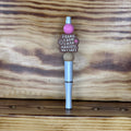 A novelty ink pen with a pink bead, a brown bead reading 'I CAME. I SAW. I HAD ANXIETY, SO I LEFT"