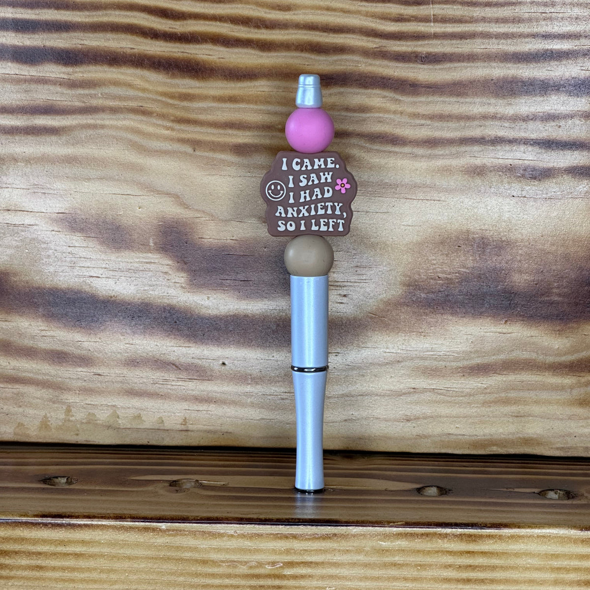 A novelty ink pen with a pink bead, a brown bead reading 'I CAME. I SAW. I HAD ANXIETY, SO I LEFT"